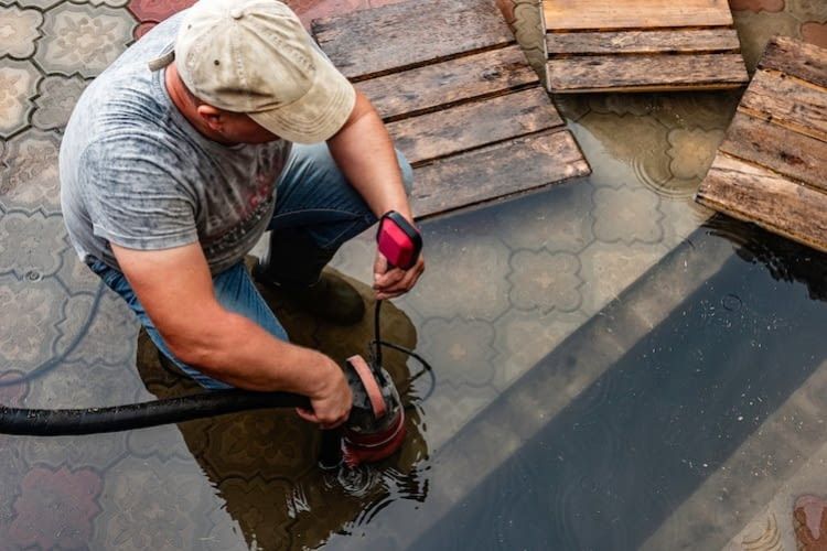 Mann saugt Wasser mit Tauchpumpe ab