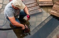 Mann saugt Wasser mit Tauchpumpe ab