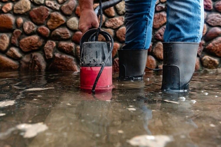 Mensch mit Gummistiefeln steht im Wasser mit einer Tauchpumpe Mensch mit Gummistiefeln steht im Wasser mit einer Tauchpumpe