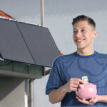 Junger Mann mit Sparschwein vor Solarmodulen
