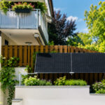 Zwei Solarmodule an einem Gartenzaun umgeben von viel Grün