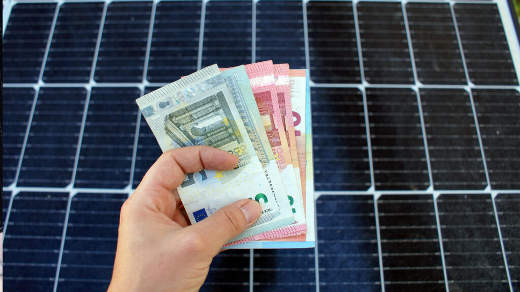 wie-hoch-sind-die-balkonkraftwerk-starter-preise-aktuell Hand mit Geldscheinen vor Solarmodul