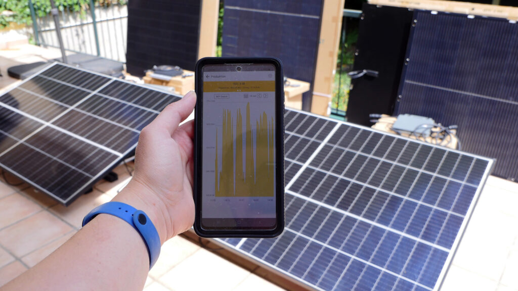 wie-viel-solaranlagfen-ertrag-liefern-balkonkraftwerke Hand hält eine App mit Ertragsgrafiken vor Solarmodule