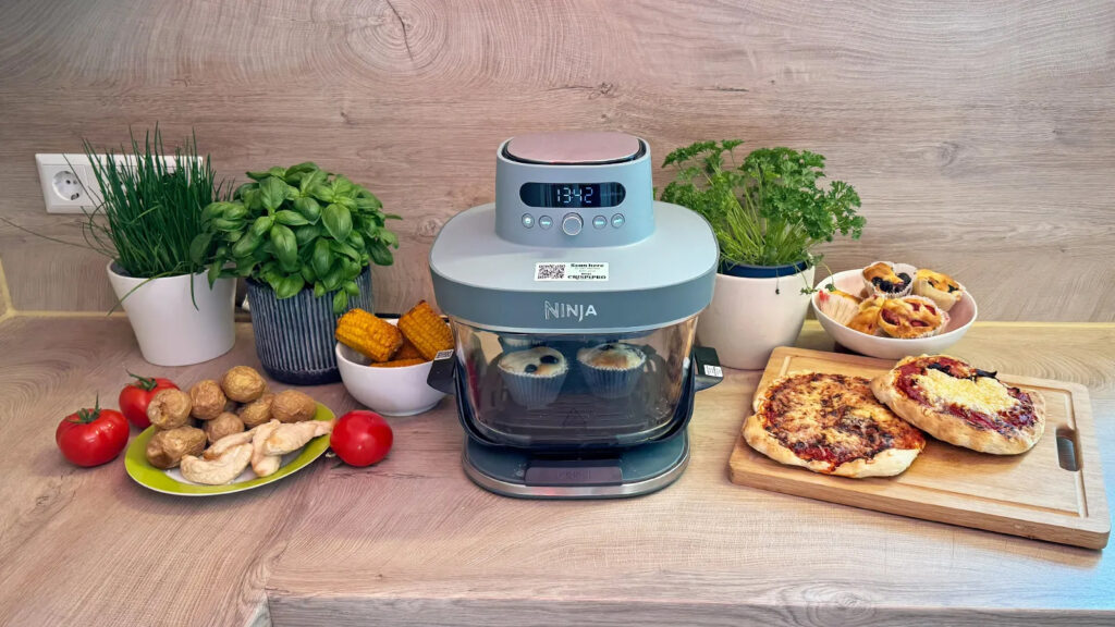 Mini-Heißluftfritteuse umgeben vpn Pizza, Muffins, Maiskolben, Putenfleisch und Kartoffeln