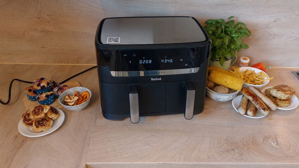 tefal-dual-easy-fry-uebersicht-der-zubereiteten-lebensmittel Doppelkammer-Airfryer umgeben von Würstchen, Mais und Muffins