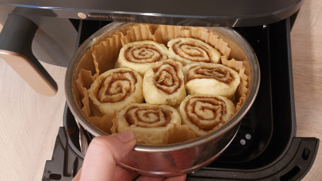 zimtschnecken-backen-in-der-heissluftfritteuse Eine Hand schiebt eine Kuchform mit Zimtschnecken in einen Airfryer