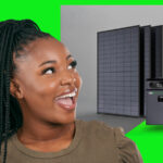 Eine Frau zeigt begeistert auf einen Stromspeicher vor 2 Solarmodulen