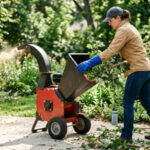 Eine Frau mit blauen Handschuhen stopft Zweige in einen Gartenhäcksler