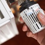 Eine Hand stellt ein Heizkörperthermostat ein.
