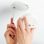 Ein Rauchmelder wird mit einem Schraubendreher an der Decke montiert.