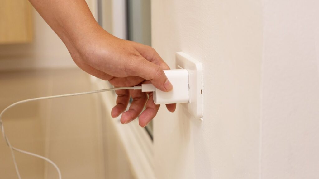Eine Hand steckt ein Handy-Ladegerät in die Steckdose.