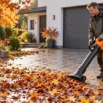 Mann saugt mit einem Akku-Laubsauger mit Stützrad nasses Herbstlaub von einer gepflasterten Einfahrt