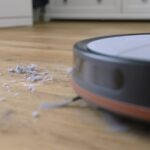 Saugroboter fährt auf Hausstaub und Haare auf einem Holzboden zu
